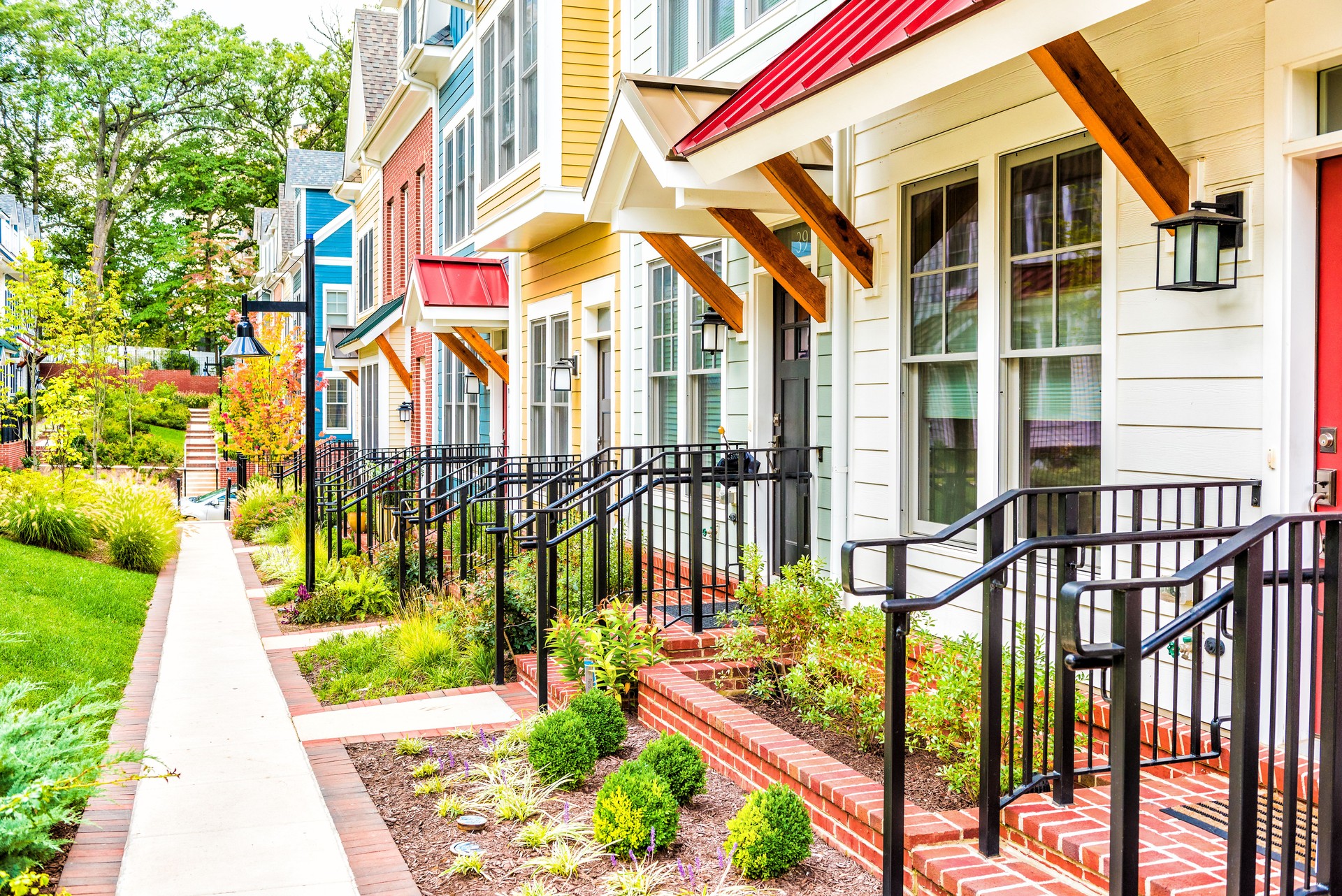 Row of colorful, red, yellow, blue, white, green painted residential townhouses, homes, houses with brick patio gardens in summer